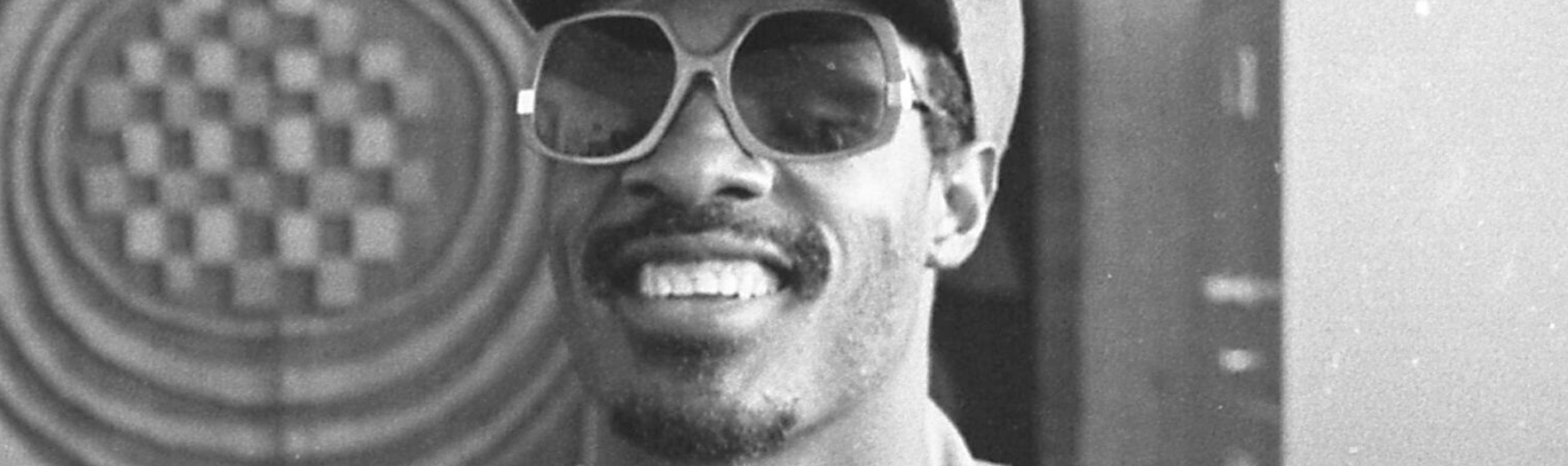Black and white photo of a Black man smiling while wearing sunglasses